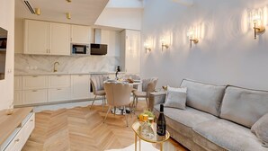 A modern living room with a sofa, a dining table with chairs, and a kitchen area with white cabinets and a microwave. - TBS 204 - Prestigious suite near Champs-Élysées (Paris)