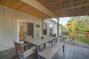 Relax on the covered patio with a bench, table, and chairs, surrounded by trees and a wooden fence.