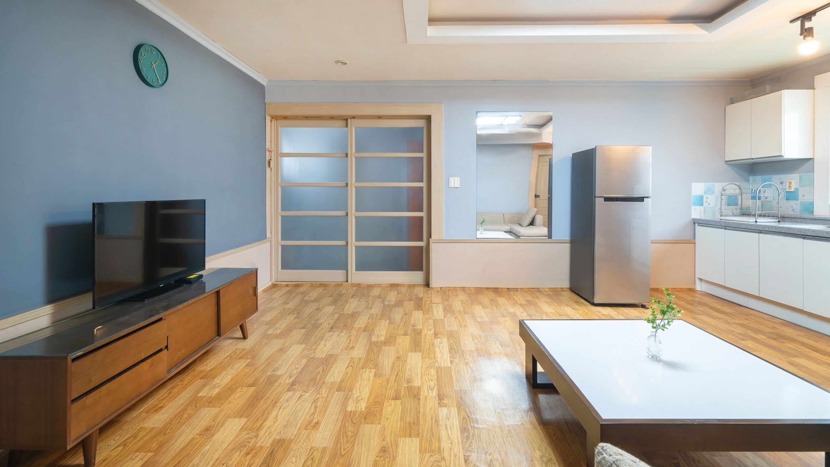 Una cocina moderna con refrigerador, una mesa de comedor y un televisor sobre un mueble de madera.