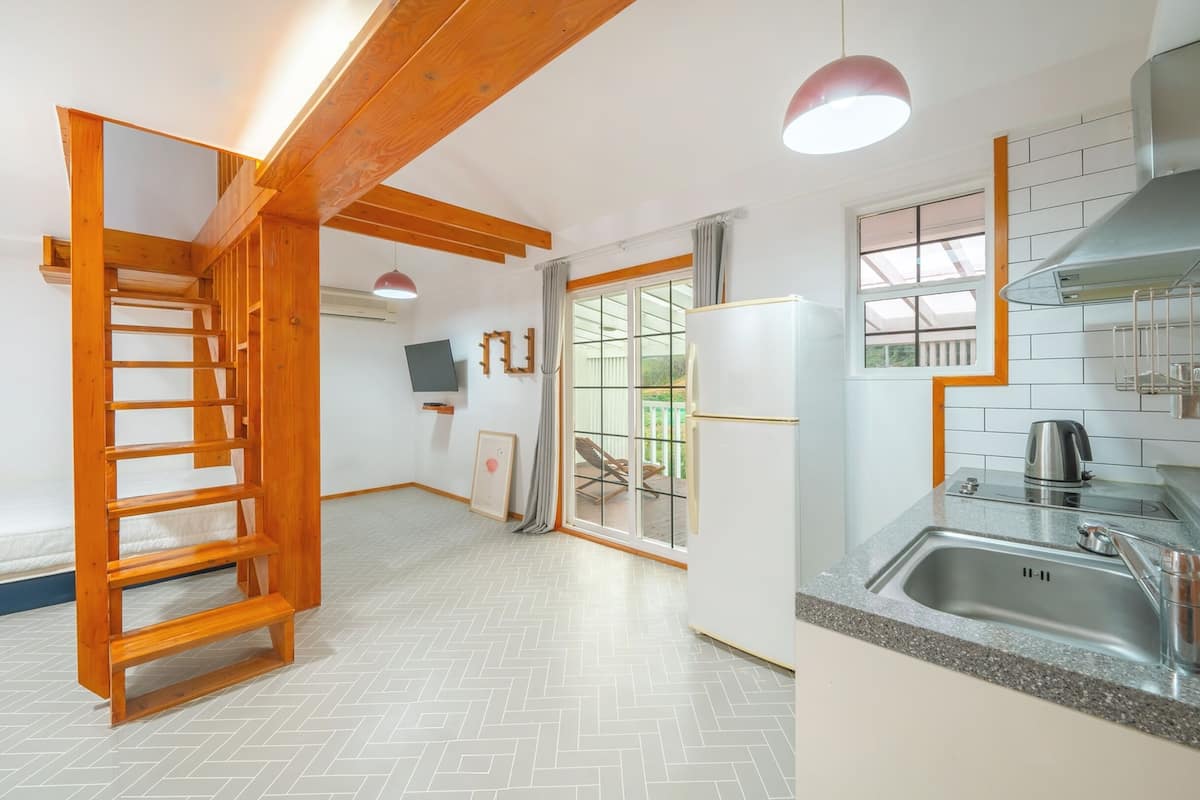 A compact kitchen with a built-in stove, a sink, and a wooden staircase leading to a balcony.