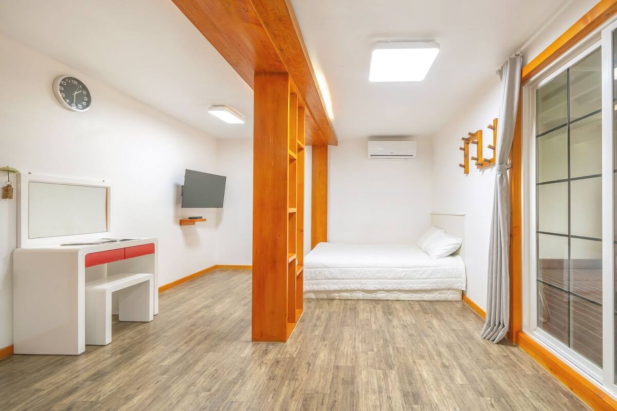 A room with a bed, a desk, a TV, and a large window.
