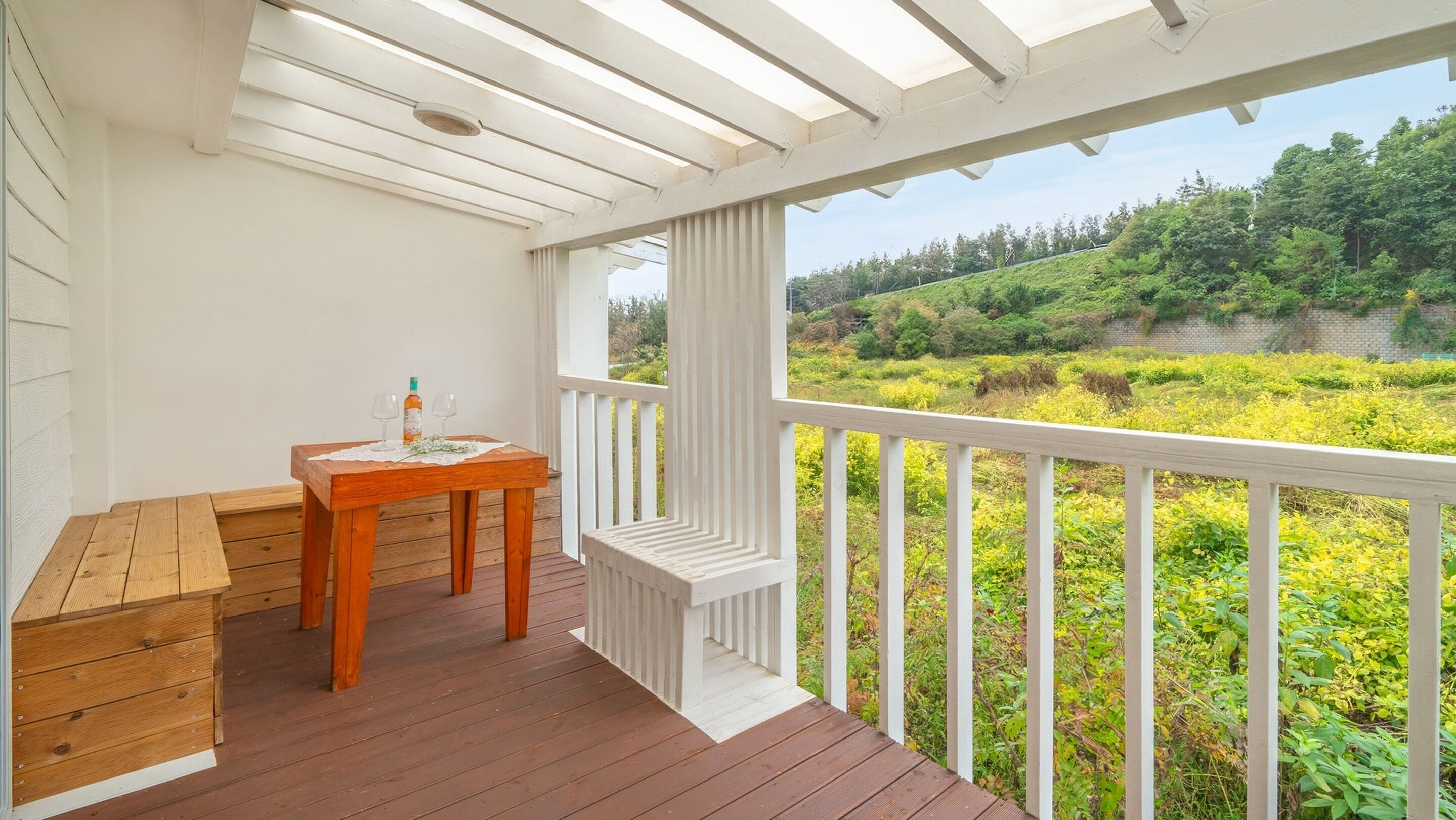 Une terrasse en bois avec une table et un banc, offrant une vue sur un paysage verdoyant et luxuriant.