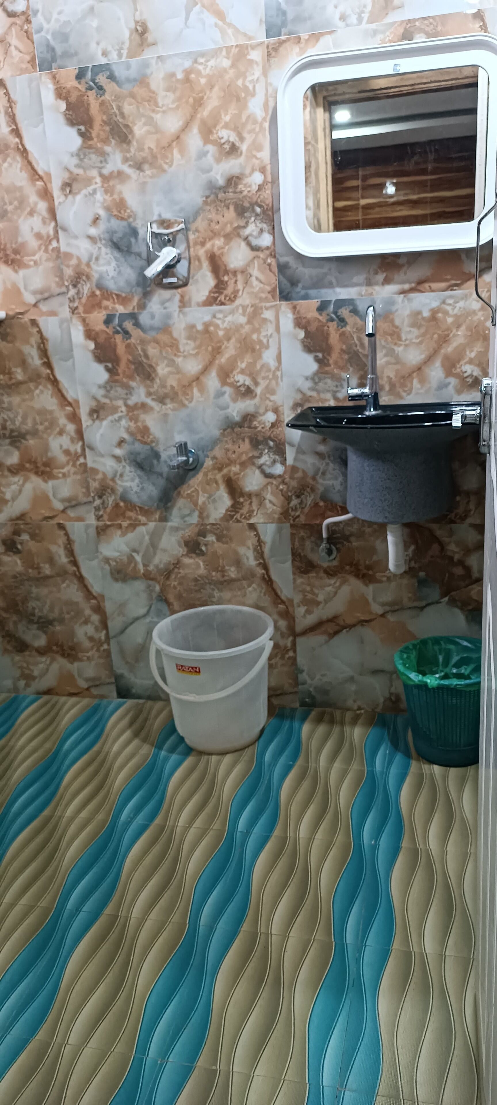 A bathroom with marble walls, a sink, a window, a white bucket, and a green trash bin.