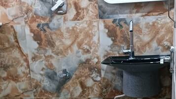 A bathroom with marble walls, a sink, a window, a white bucket, and a green trash bin.