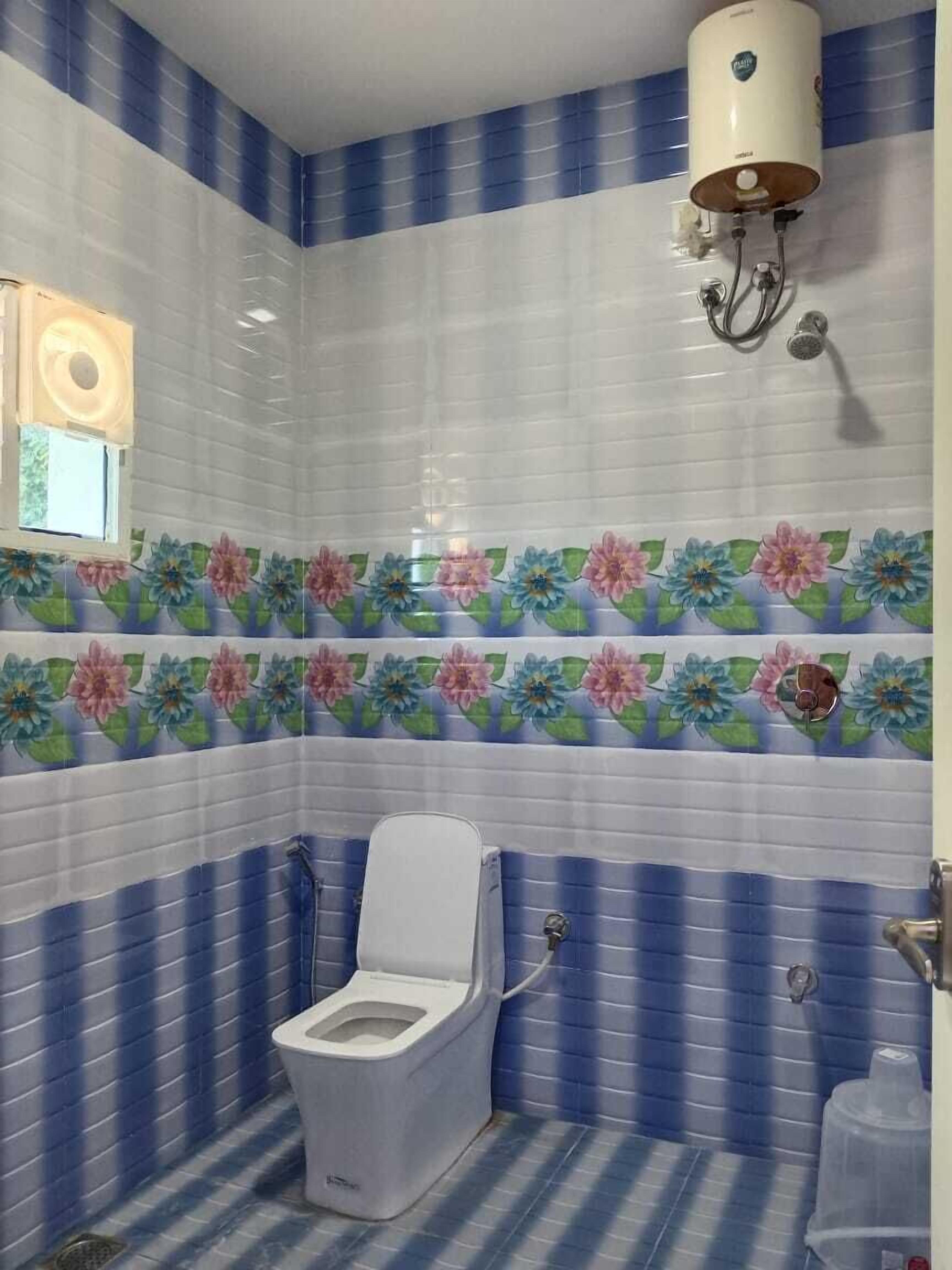 Un baño con azulejos blancos y azules a rayas, un inodoro y un calentador de agua en la pared.