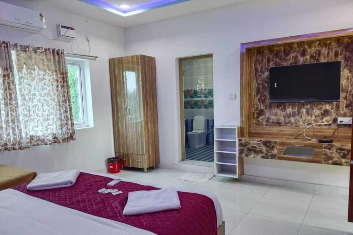 Habitación de hotel con dos camas, un televisor montado en una pared de piedra, un armario y una pequeña zona de estar.