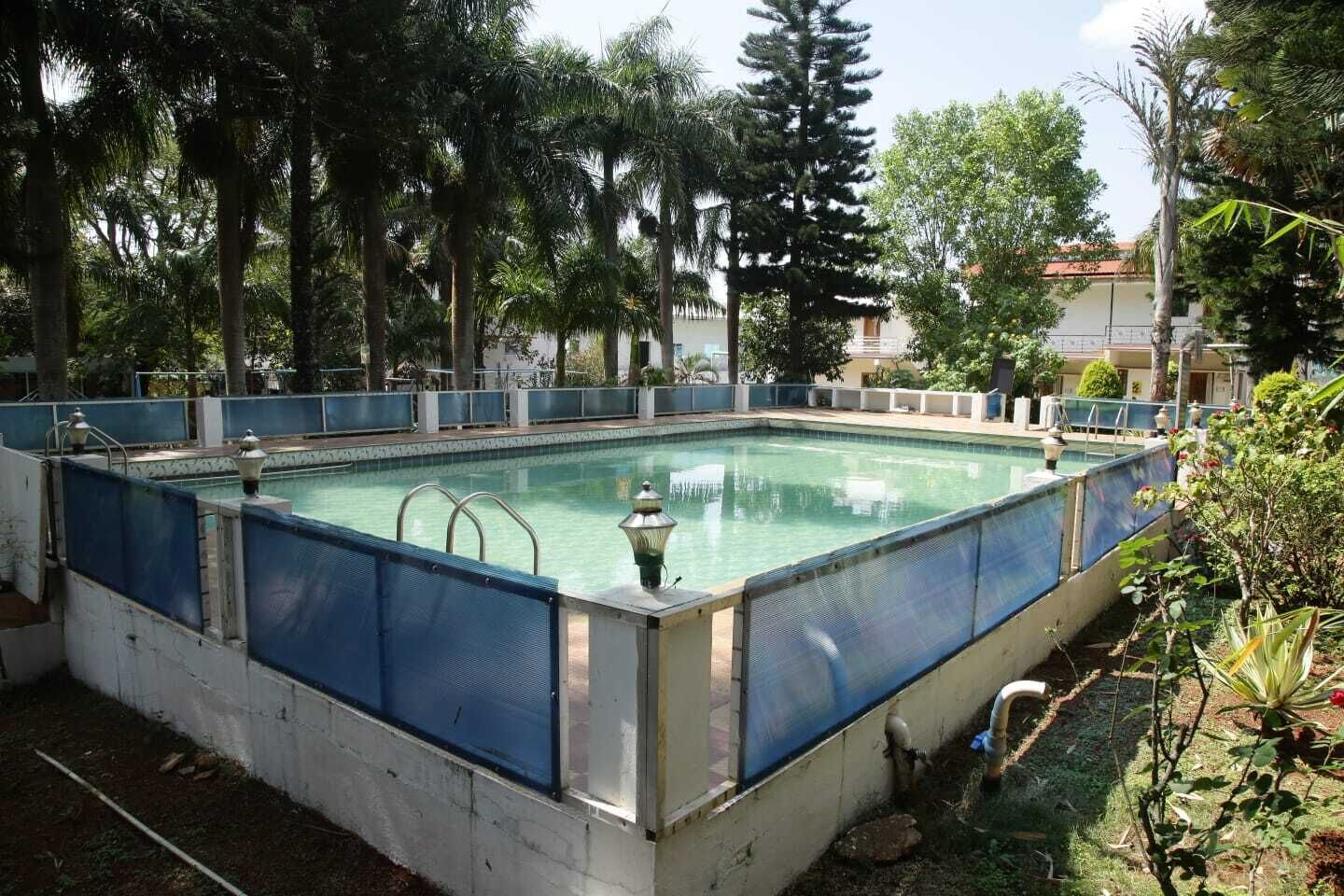 Une piscine extérieure rectangulaire, entourée d’arbres et de végétation, et protégée par une clôture de sécurité bleue.