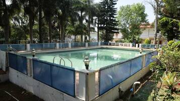 A rectangular outdoor swimming pool with a blue safety fence, surrounded by trees and vegetation.