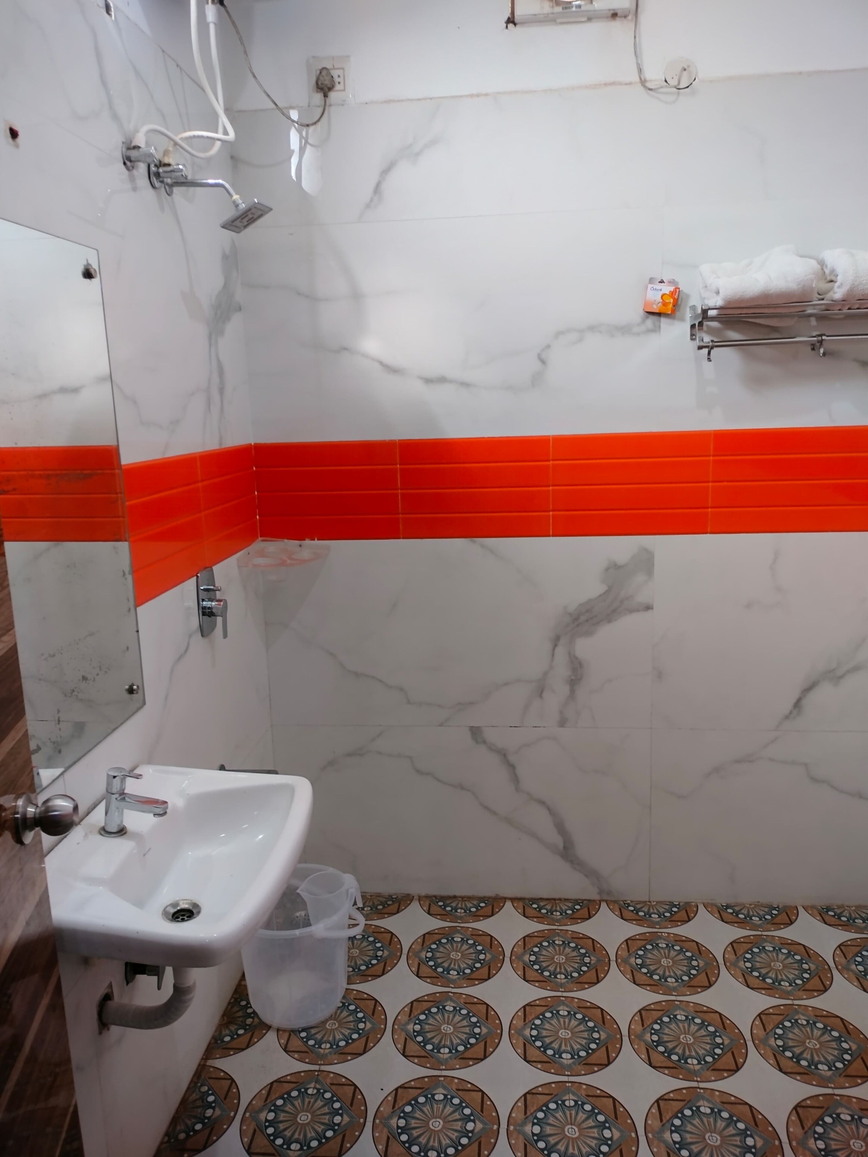 A bathroom with a white sink, a mirror, a shower with a handheld showerhead, and a red-tiled shower enclosure.