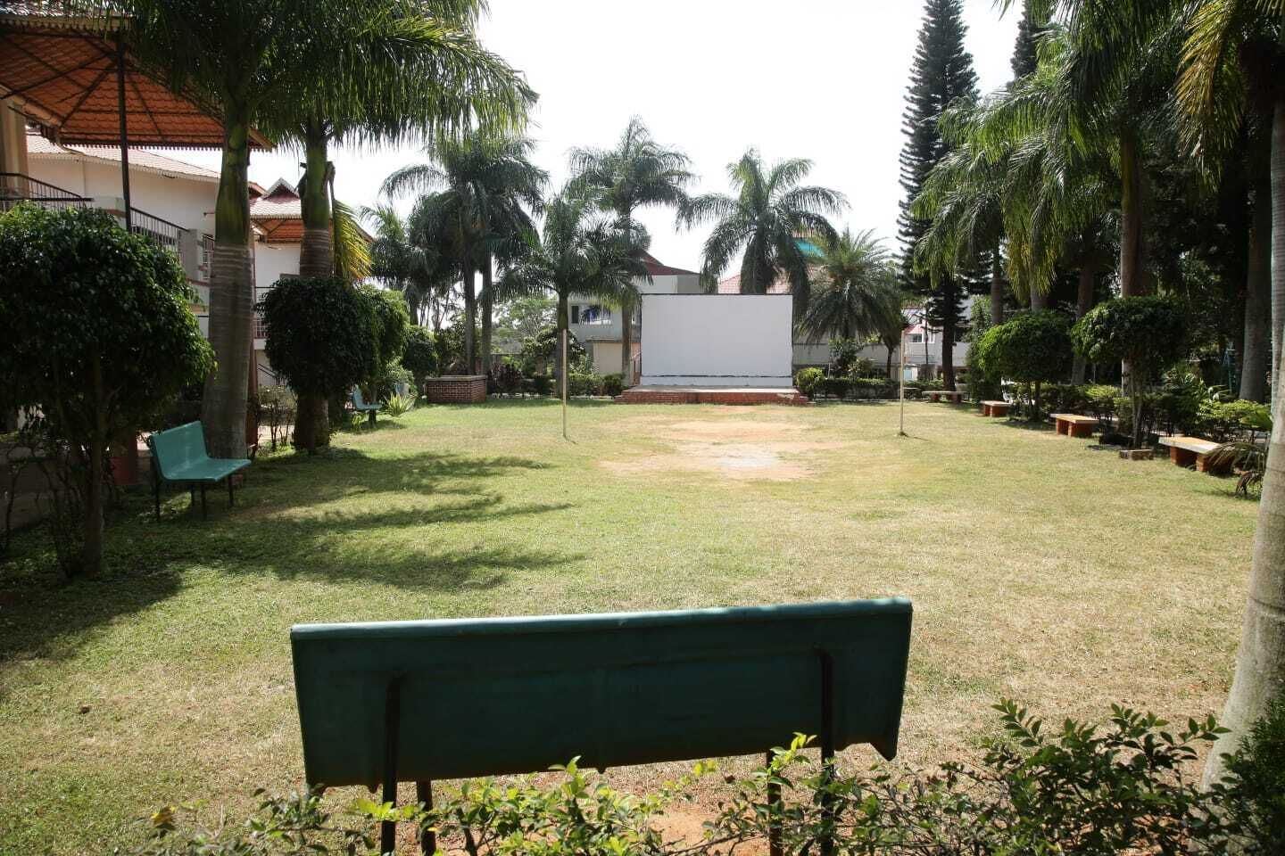 A grassy courtyard with a bench, palm trees, and a building in the background.