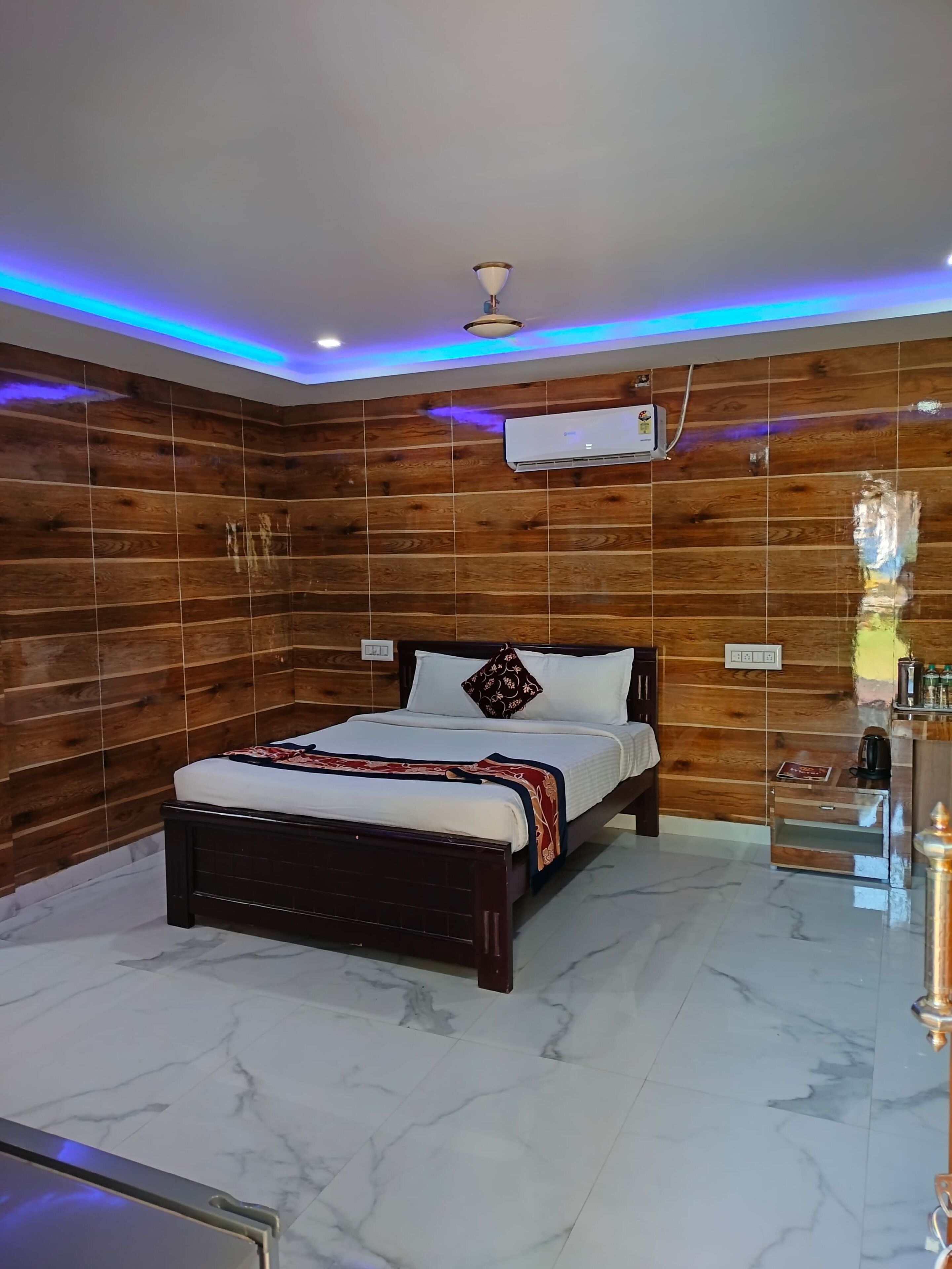 A bedroom with a wooden wall panel design, a bed with a patterned bedspread, and a marble floor.