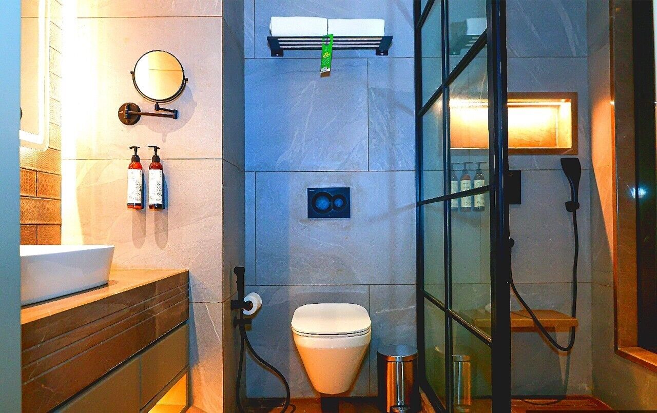 Een moderne badkamer met een douchecabine van glas, een toilet en een wastafel met spiegel en twee flessen shampoo.