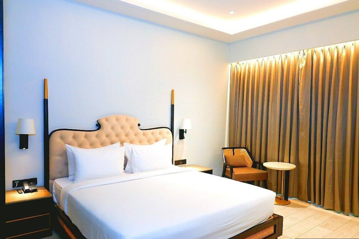 A hotel room with a large bed, two bedside tables with lamps, a chair, and a curtain.