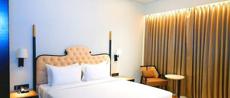 Una habitación de hotel con una cama grande, dos mesitas de noche con lámparas, una silla y una cortina.