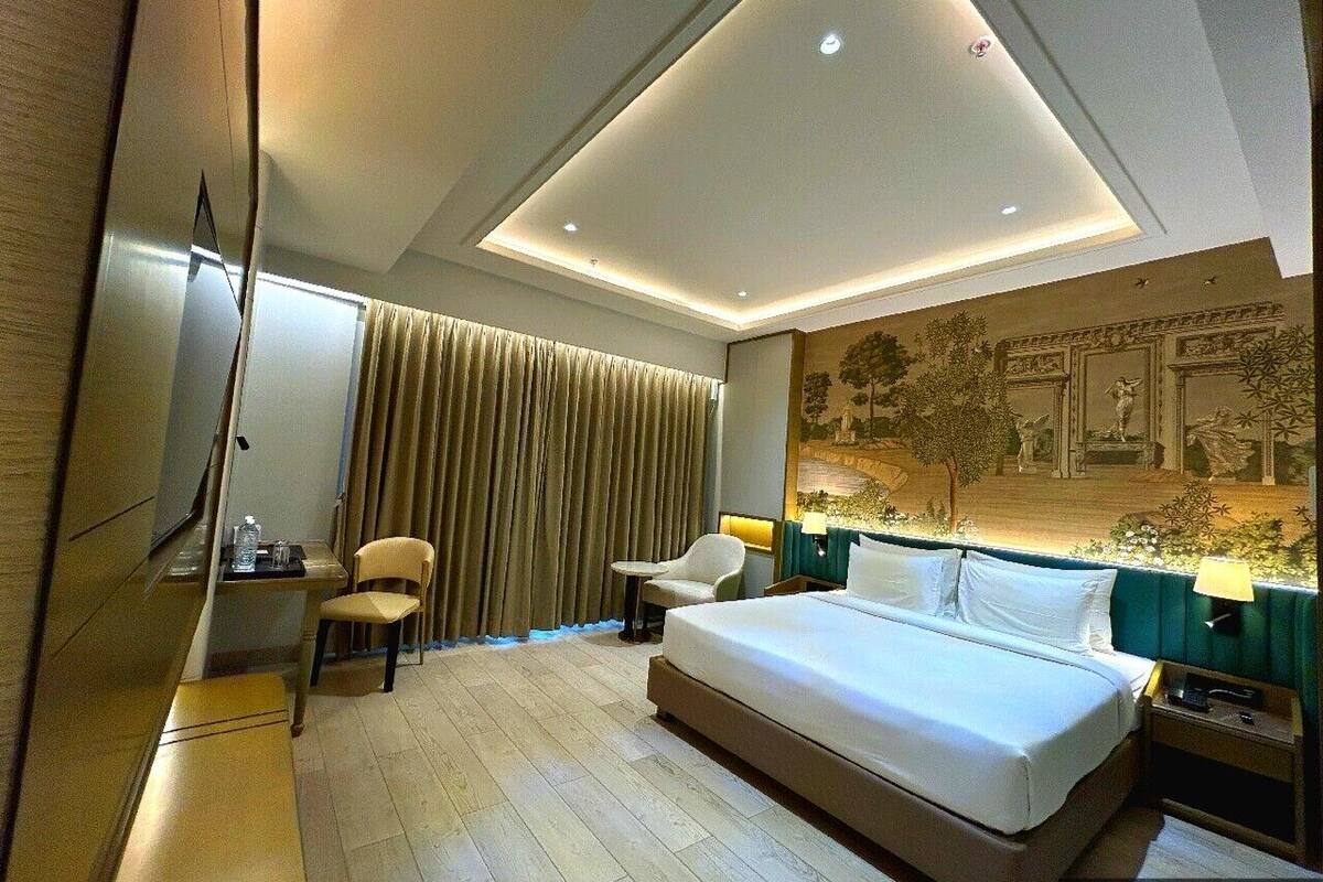 A modern hotel room with a large bed, a desk with a chair, a TV, and a wall with a mural.