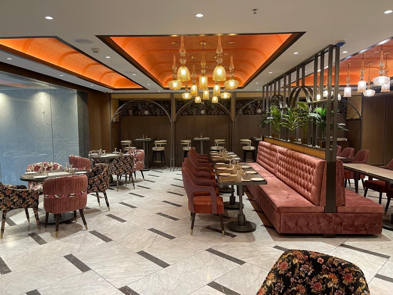 A spacious restaurant with a long red bench seating area, multiple tables, and a chandelier.