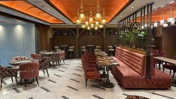 Un ristorante spazioso con una lunga panca rossa, diversi tavoli e un lampadario.