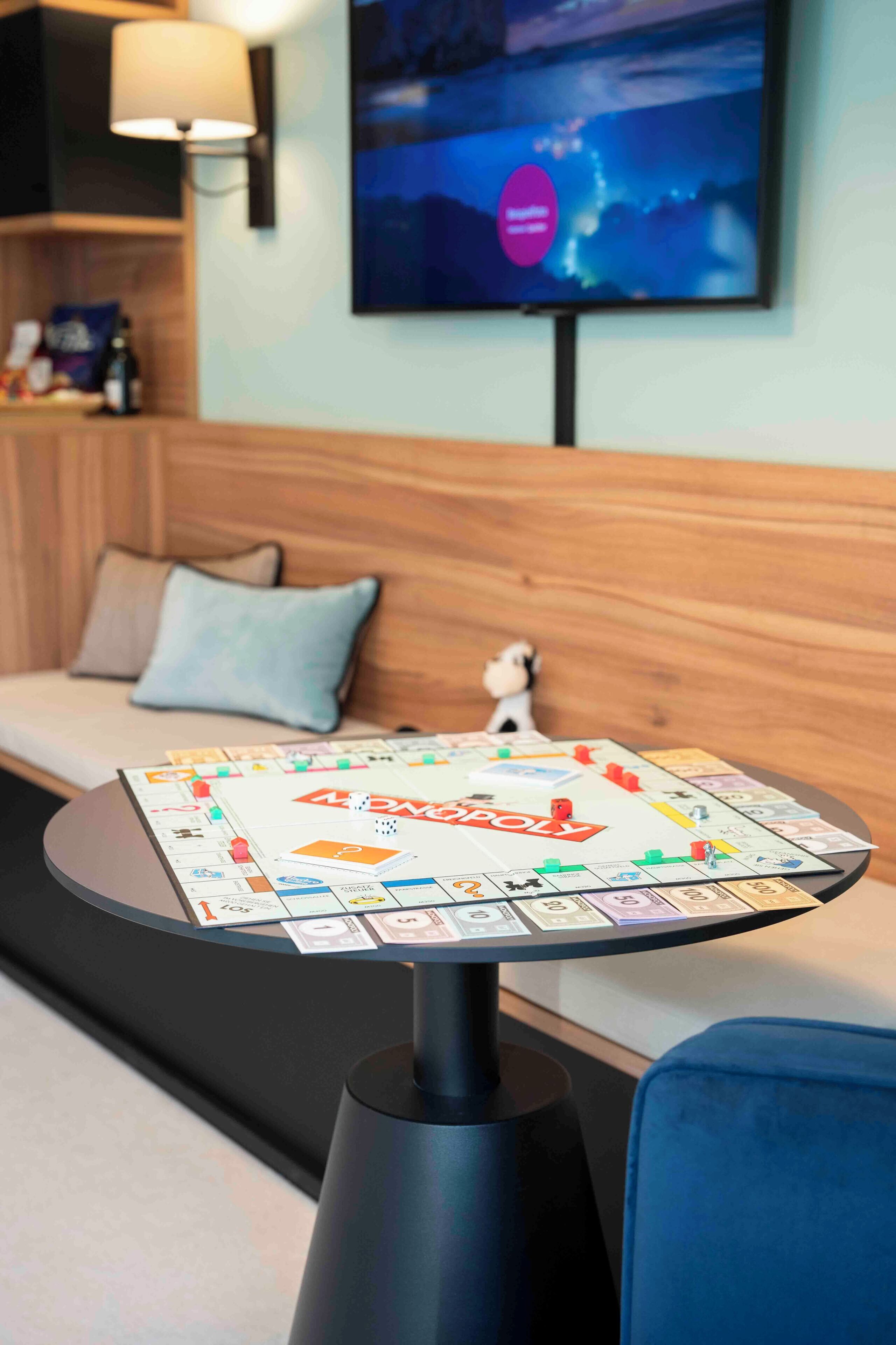 A board game table in a hotel room with a sofa and a television in the background.