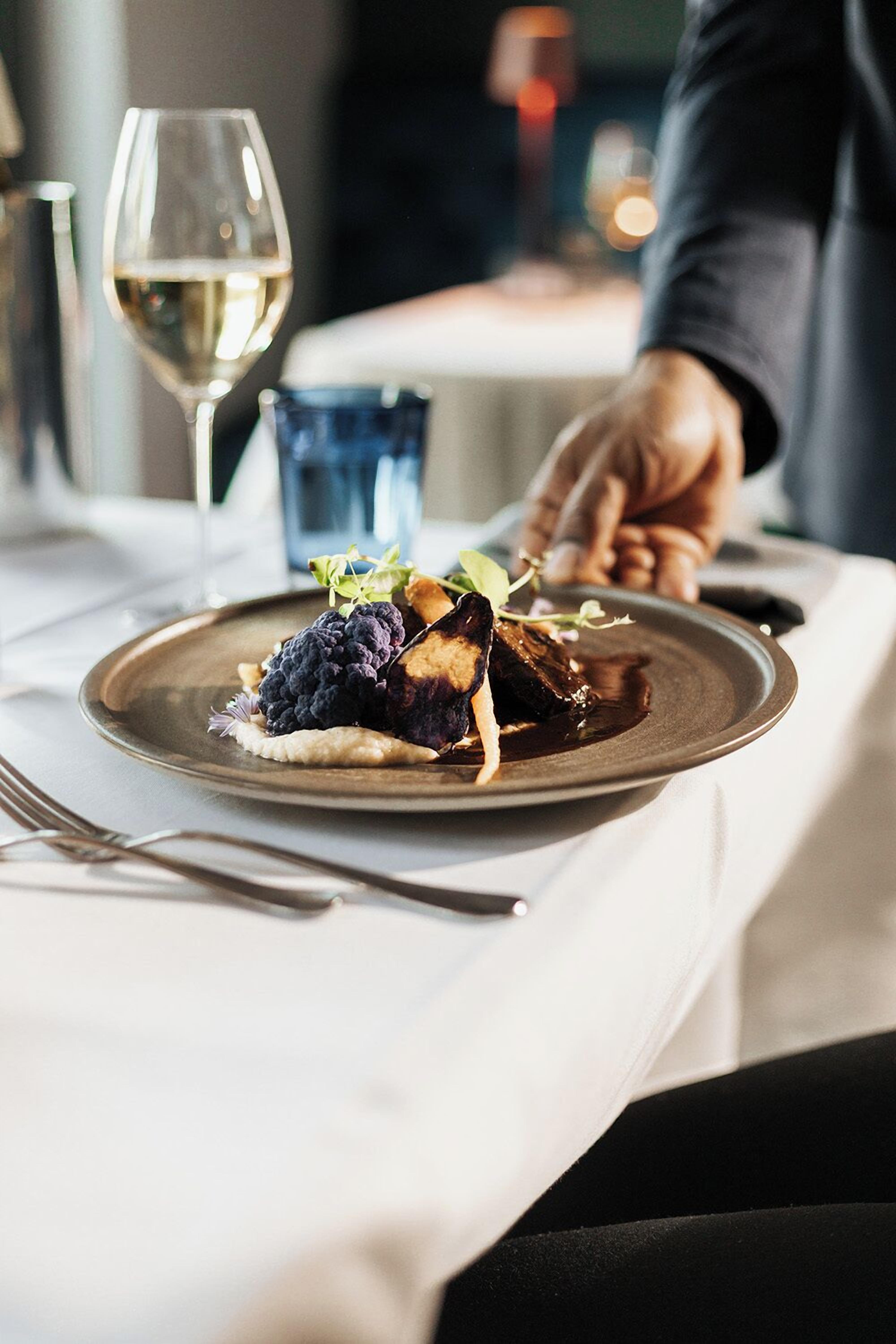 A dining table with a plate of food, a wine glass, and a blue cup.