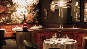 A restaurant with a round table set for dining, a red upholstered booth, and a decorative chandelier. - The Great North - Hotel (Kaltenkirchen)