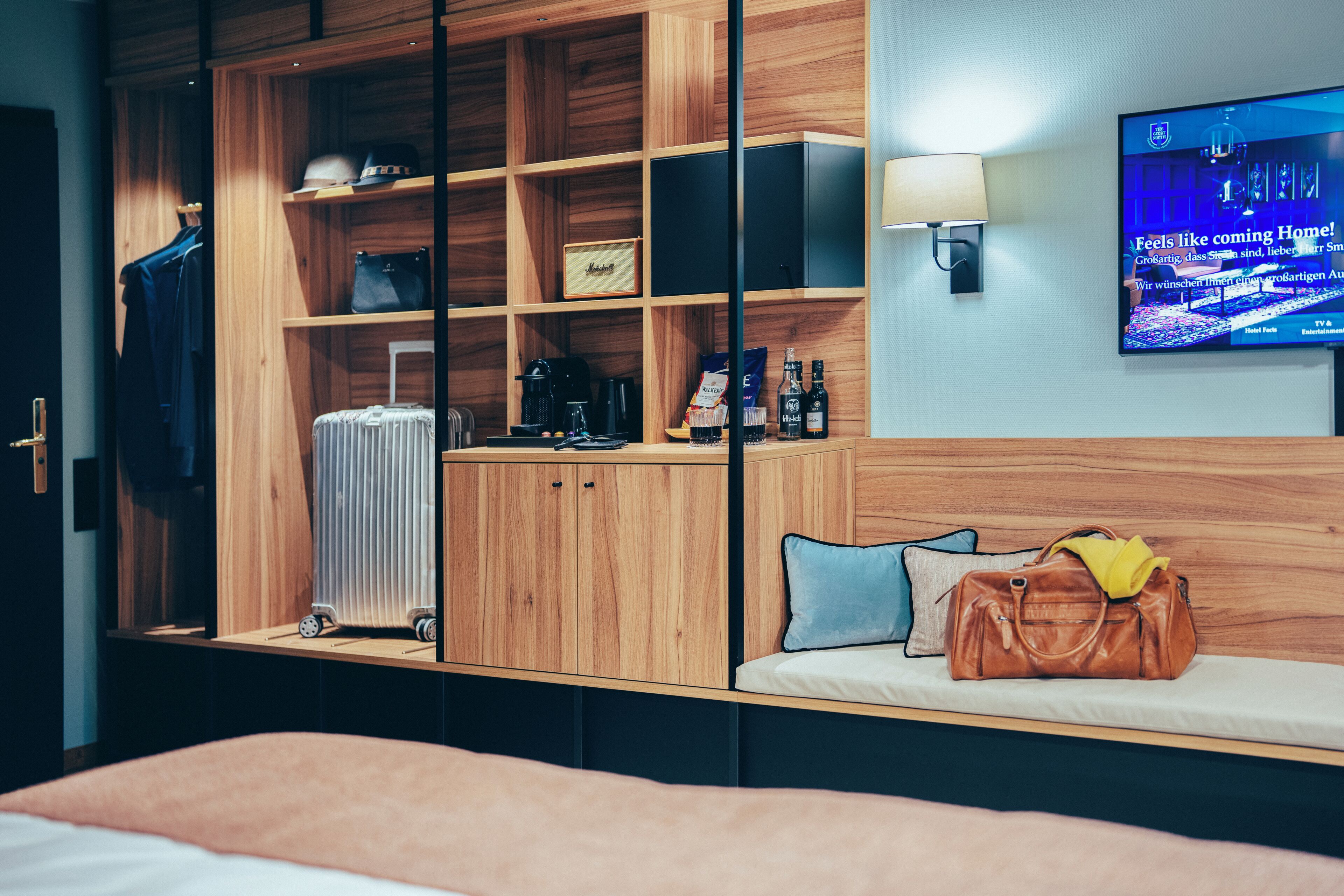 A hotel room with a bed, a TV, a wooden wardrobe, a suitcase, and a handbag.