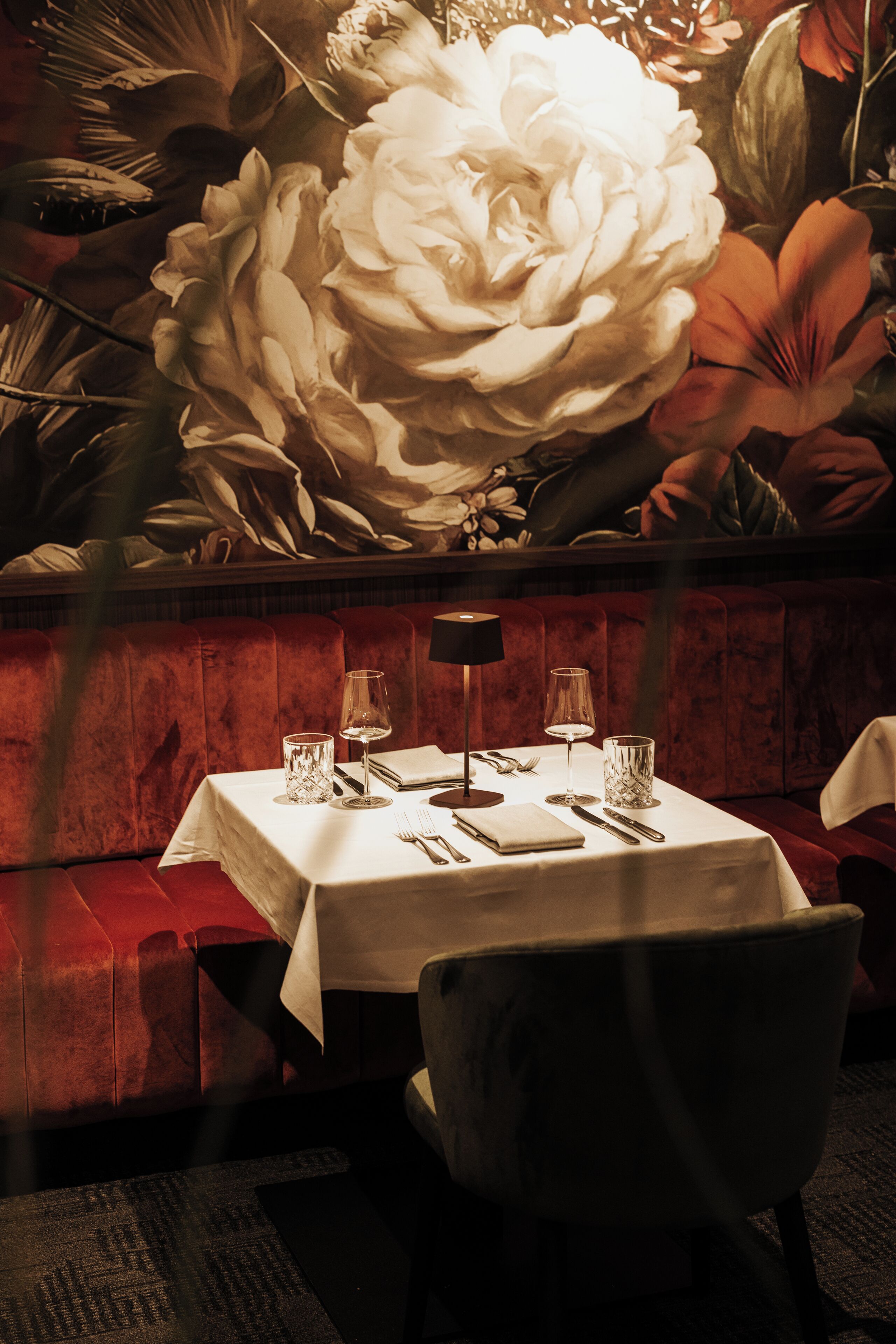 Mesa de comedor cubierta con un mantel blanco, rodeada de asientos de terciopelo rojo.