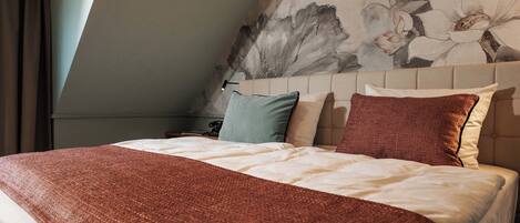 Un dormitorio con cama, almohadas, cabecero y una pared con un mural floral.