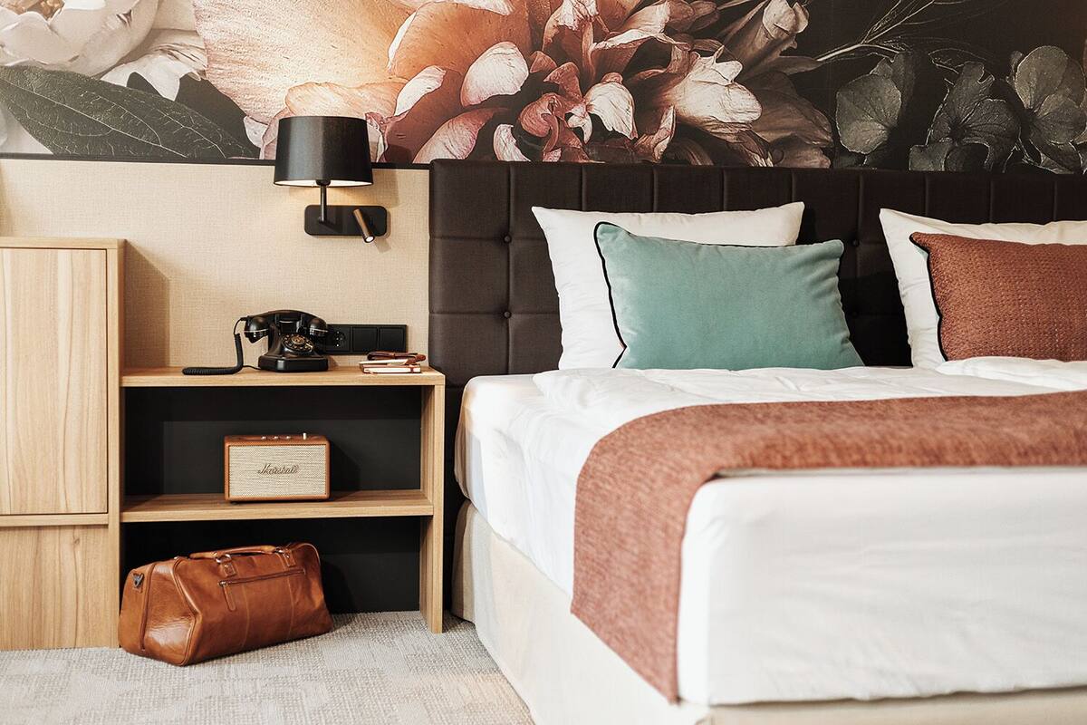 A neatly arranged hotel room with a bed, a nightstand with a lamp, a telephone, and a vintage radio.