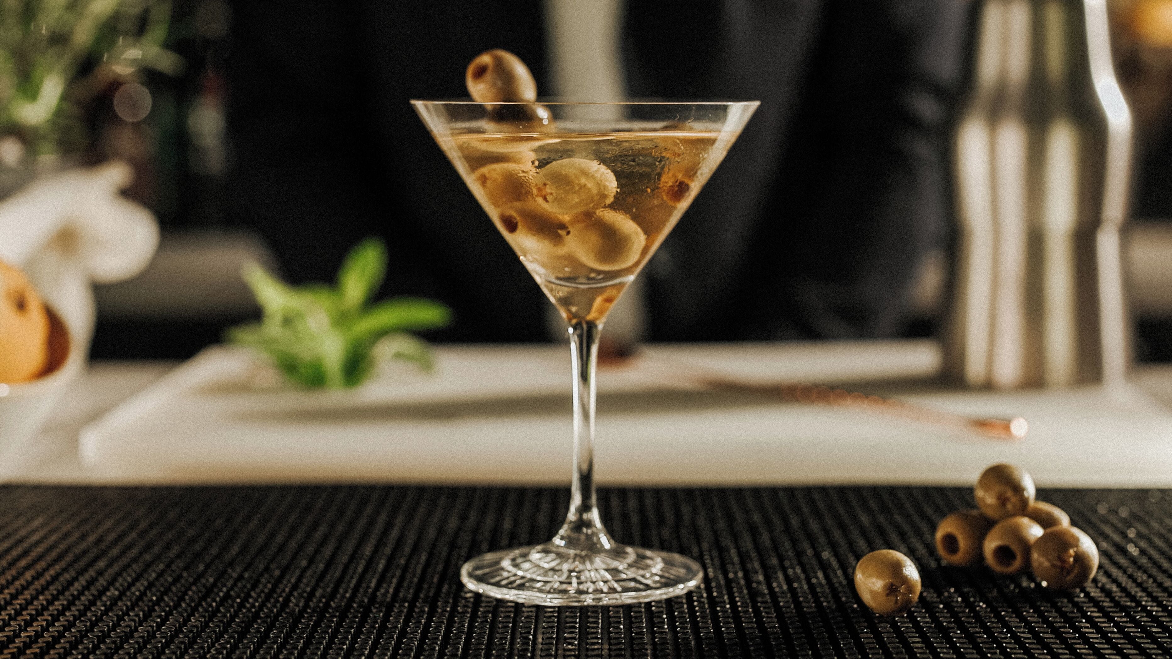 A martini glass with olives on a textured surface.