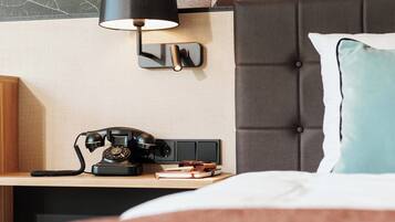 A hotel room with a bed, a nightstand with a telephone, a wall-mounted lamp, and a decorative wall.