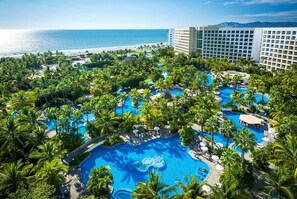 Un resort con varias piscinas rodeadas de palmeras, una playa y un gran edificio de hotel.