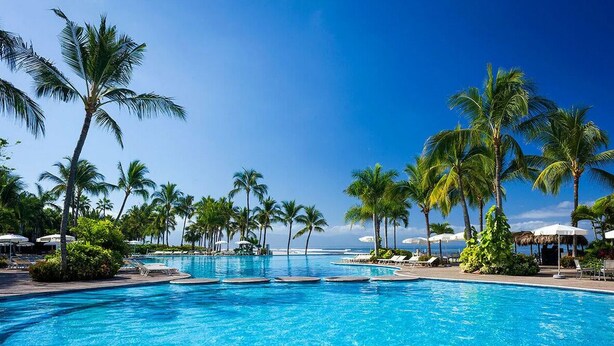 A large outdoor swimming pool surrounded by palm trees and lounge chairs, with a clear view of the ocean in the background. - 3 Bedroom Spa Tower 5 Diamond VIP Golf Tournament VIP Park Access Vidanta World (Nuevo Vallarta)