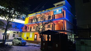 Un edificio de varios pisos con un cartel que dice 'Krystal Inn', indicando que es un hotel. Hay un automóvil estacionado frente al edificio, que tiene balcones y una escalera visible.