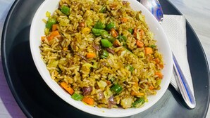 Un plato de arroz frito con verduras sobre una fuente negra, acompañado de una cuchara y una servilleta.