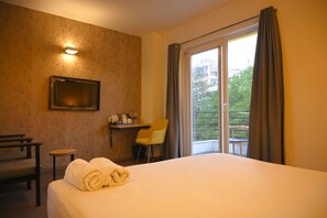 Habitació d'hotel amb llit, escriptori, cadira, televisió i un balcó amb cortines.