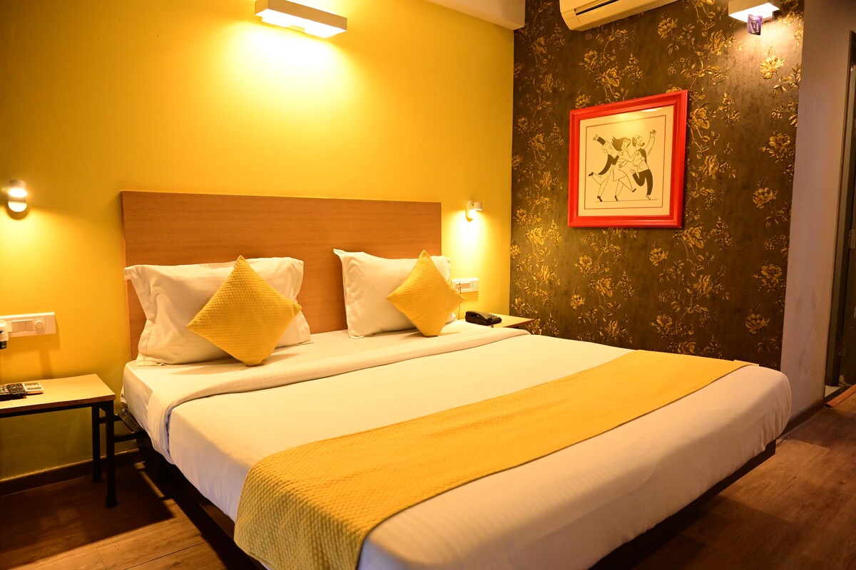 A hotel room with a large bed, two bedside tables, a nightstand, a framed picture on the wall, and a floral wallpaper pattern.