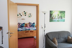 Una habitación con una cama, un sofá gris, una lámpara de pared y un cuadro enmarcado.