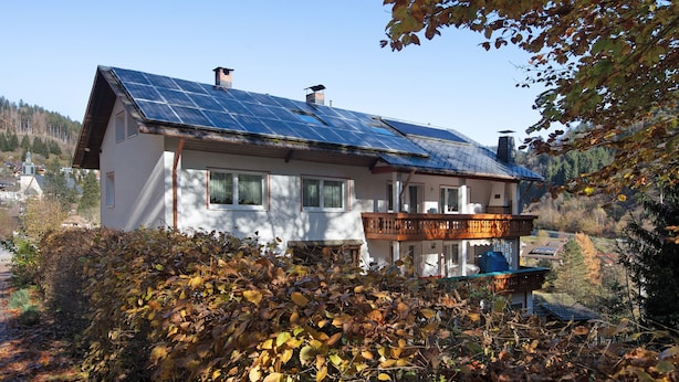A house with a solar panel roof, a balcony, and a garden with autumn foliage. - Appartement Nr 5 mit Gemeinschaftsterrasse, Garten und WLAN (Todtmoos)