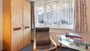 A room with a brown leather chair, a glass table with a book and a pink notebook, and a wooden wardrobe. - Appartement Nr 5 mit Gemeinschaftsterrasse, Garten und WLAN (Todtmoos)
