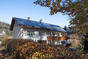Une maison avec un toit équipé de panneaux solaires, un balcon et un jardin aux couleurs automnales.