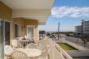 A balcony with a table and chairs, a view of the street, and a building across the street.