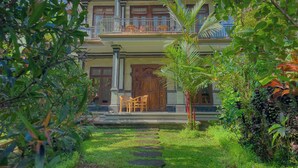 A two-story building with a balcony, a wooden door, and a garden with a pathway. - Surya Ubud View and Suites by EPS (Tegallalang)