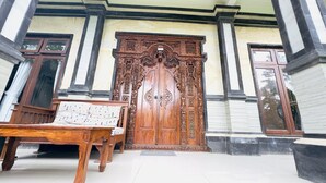 A wooden bench and a large ornate door in front of a building with a tiled floor. - Surya Ubud View and Suites by EPS (Tegallalang)