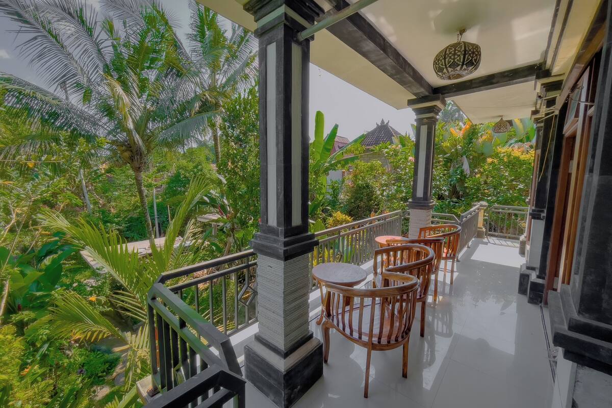 Ein Balkon mit Holzstühlen und einem Tisch, umgeben von üppiger Vegetation und Blick auf ein traditionelles Gebäude.