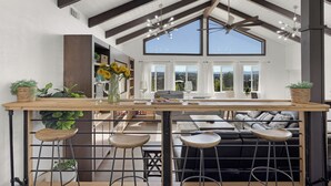 A modern kitchen with a wooden island, bar stools, and a seating area with a sofa and cushions. - Paso Vista Bella by AvantStay | Luxe Group Escape w/ Wine Country Views (Paso Robles)
