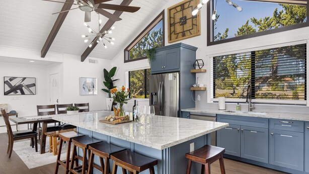 A modern kitchen with a large island, bar stools, and a view of trees through the windows. - Paso Vista Bella by AvantStay | Luxe Group Escape w/ Wine Country Views (Paso Robles)