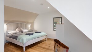 A bedroom with a sloped ceiling, a bed with a headboard, a bedside table, and a wall-mounted mirror. - Apartment 'Louisenkate' with Private Terrace, Private Garden and Wi-Fi (Pellworm)