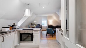 A modern kitchen with white cabinetry, a central island, and a dining area with chairs and a table. - Apartment 'Louisenkate' with Private Terrace, Private Garden and Wi-Fi (Pellworm)
