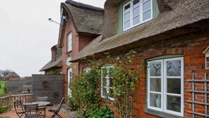 A brick house with a thatched roof, a wooden fence, and a patio with outdoor furniture. - Apartment 'Louisenkate' with Private Terrace, Private Garden and Wi-Fi (Pellworm)