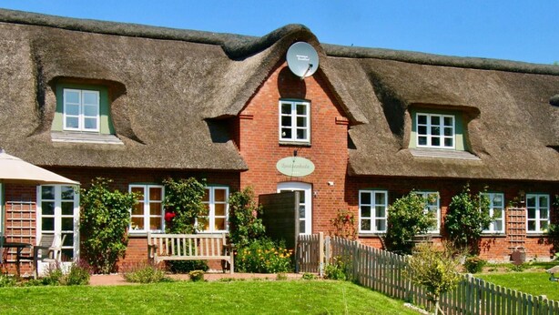 A traditional thatched-roof building with a central entrance, windows, and a satellite dish. - Apartment 'Louisenkate' with Private Terrace, Private Garden and Wi-Fi (Pellworm)